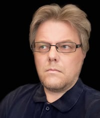 Kasvokuva Senior UX-suunnittelija Jarmo Parkkisesta mustaa taustaa vasten päällään tummansininen kauluspaita ja mustat silmälasit.