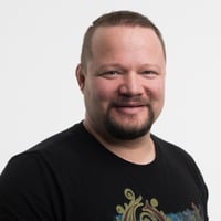 A picture of Juri Ahokas smiling to the camera against a white background wearing a black t-shirt.