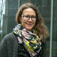 Johtava UX-suunnittelija, Elina Saarinen, päällään tummanharmaa villatakki ja kaulassaan monivärinen kaulahuivi ja päässään silmälasit.